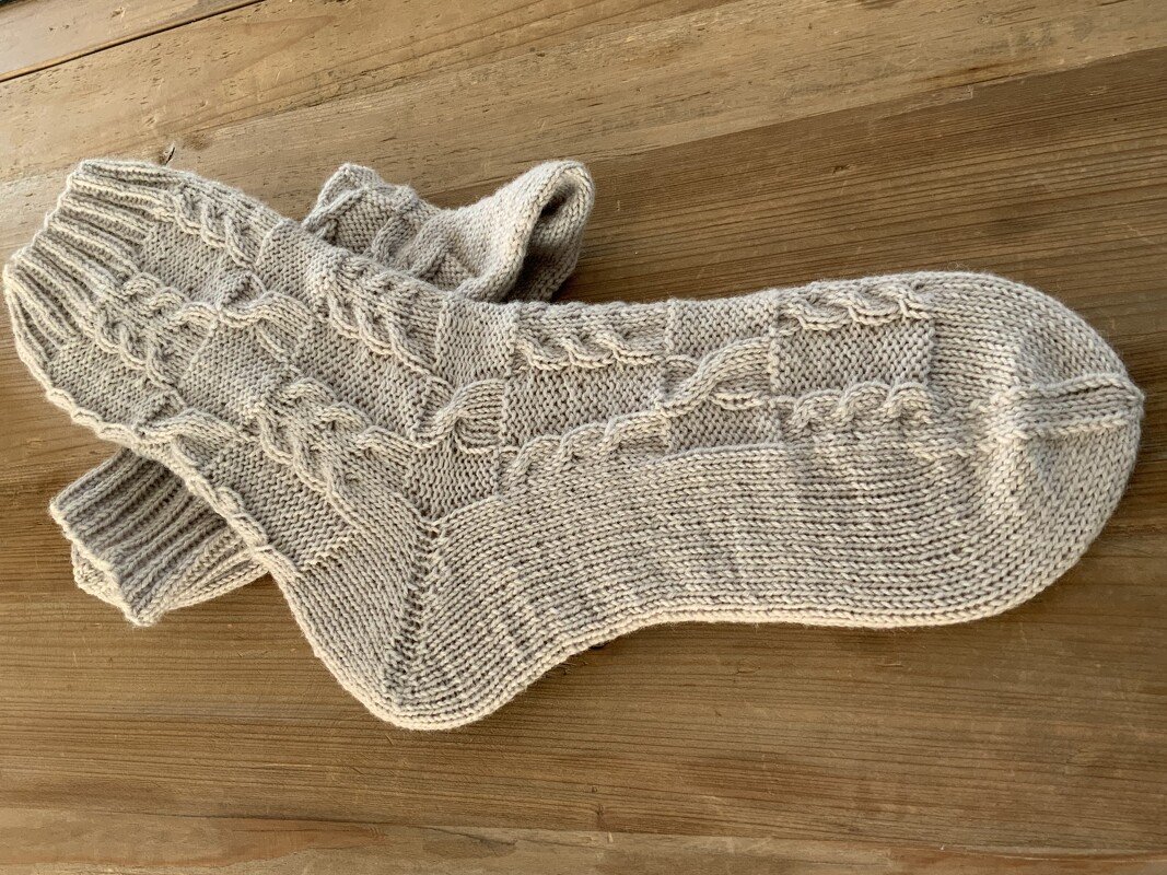 Beige handgestrickte Socken mit Zopfmuster auf Holzfläche