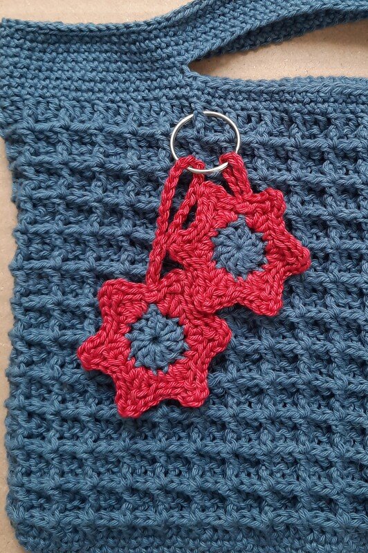 Blaue gehäkelte Henkeltasche mit zwei roten sternförmigen Anhängern an Metallring