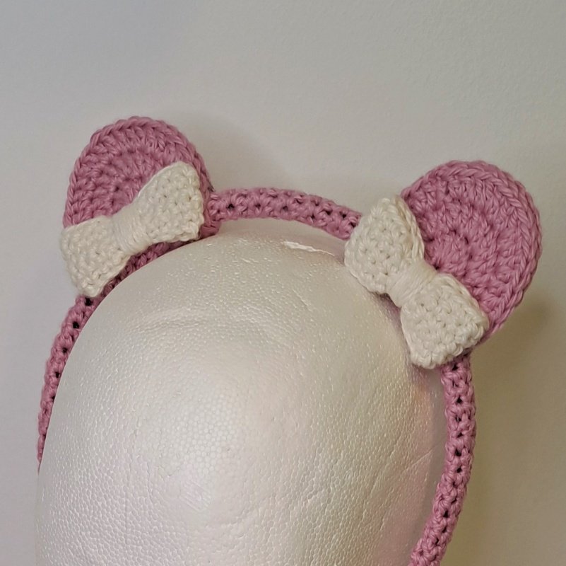 Rosa gehäkeltes Kinderstirnband mit zwei Katzenohren und weißen Schleifen