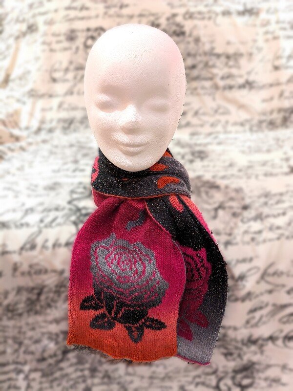 Knitted scarf with fuchsia, black, and orange rose motif on a white mannequin head.