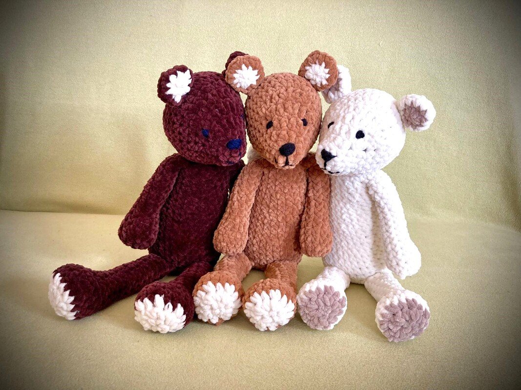 Drei handgehäkelte Amigurumi-Teddys in bordeaux, hellbraun und weiß nebeneinander