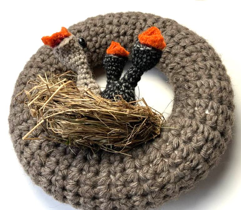 Gehäkelter runder Türkranz in Naturgrau mit Stroh‑Nest und drei dunklen Stängeln mit orangefarbigen Spitzen