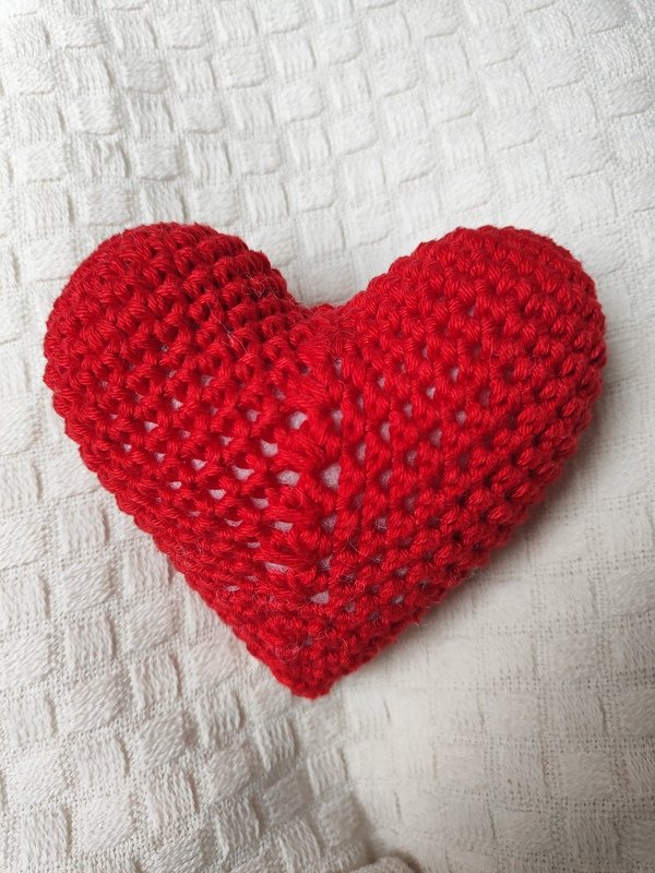 Rotes gehäkeltes Amigurumi-Herz auf weißem, strukturiertem Stoff