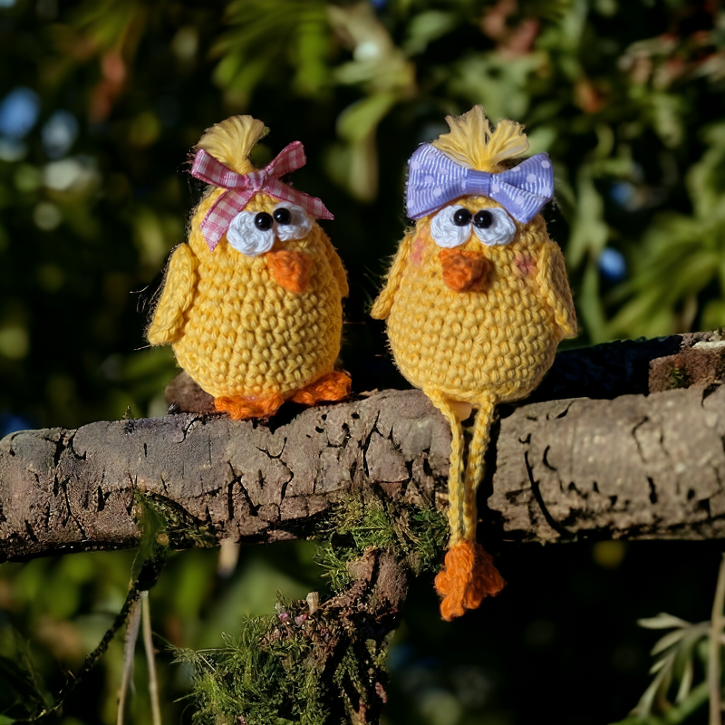 Zwei gelbe Amigurumi-Küken mit Schleifen auf einem Ast