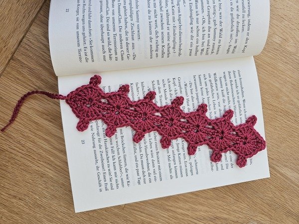 Gehäkeltes Lesezeichen in Dunkelrosa im Raupenmuster in geöffnetem Buch