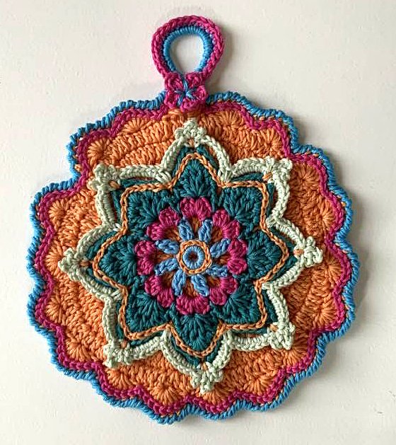 Runder, bunter, handgehäkelter Topflappen mit komplexem Mandala‑Muster in Orange, Türkis, Pink und Hellblau, mit Aufhängeschlaufe