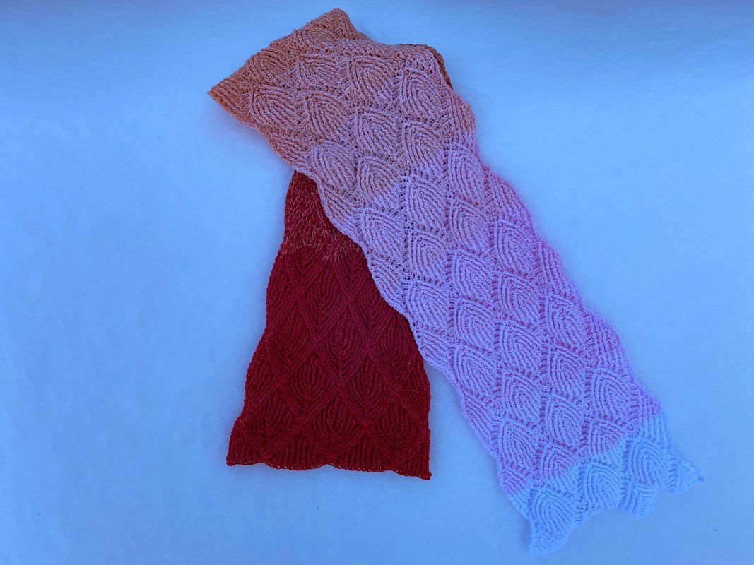 Crocheted scarf laid flat with repeating leaf-shaped textured stitches, pink-to-white gradient section overlapping a deep red section