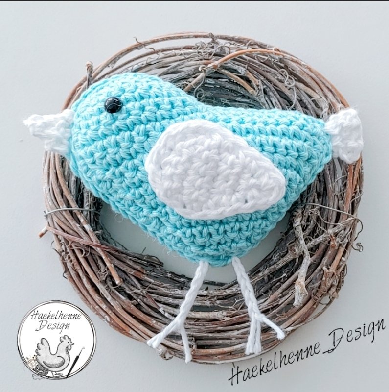 Pastellblauer Amigurumi-Vogel mit weißen Flügeln im Naturkranz