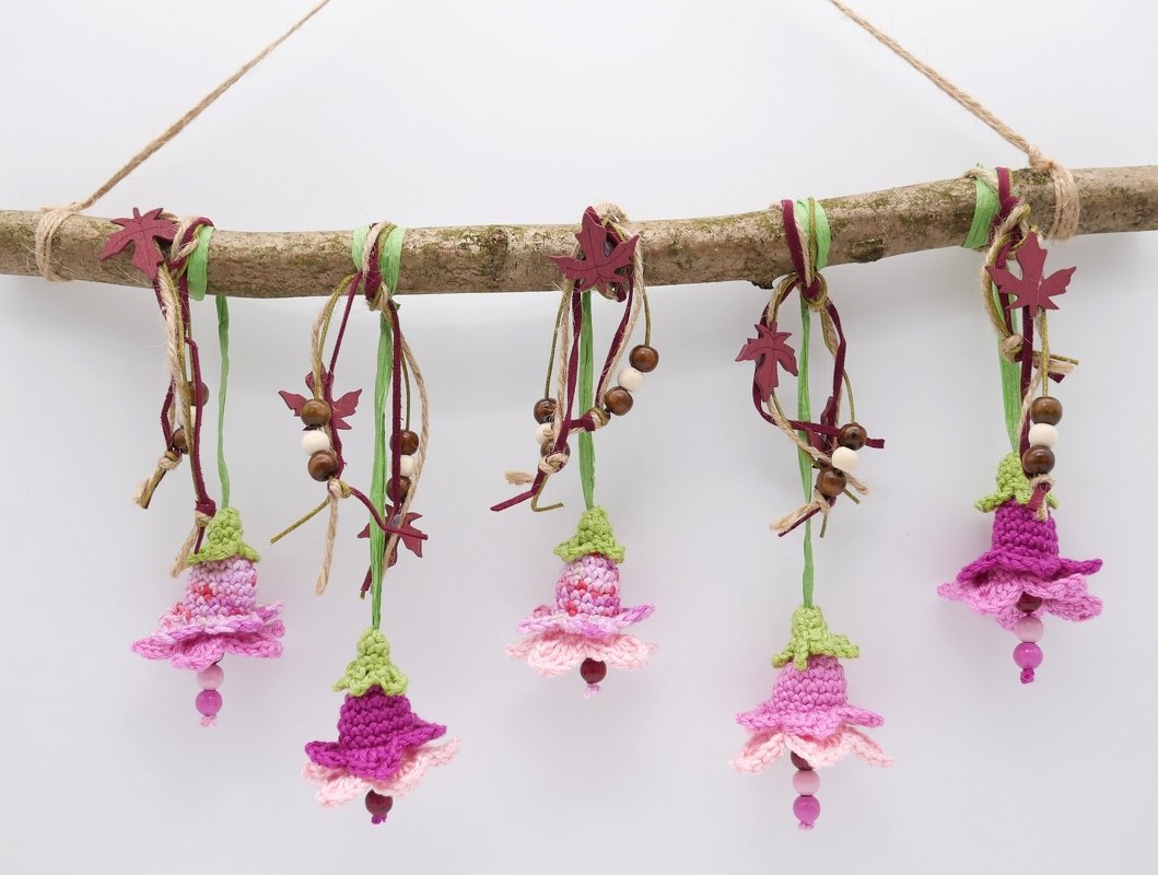 Fünf gehäkelte Blumenanhänger in Rosa und Lila an einem Ast mit Perlen und Bändern