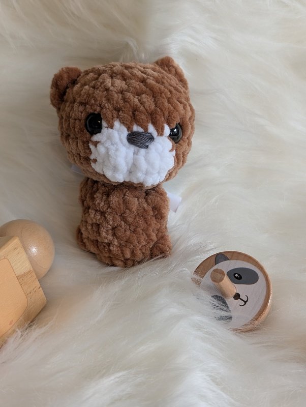 Nahaufnahme eines kleinen braunen Amigurumi-Teddybärs mit weißer Schnauze und schwarzen Augen