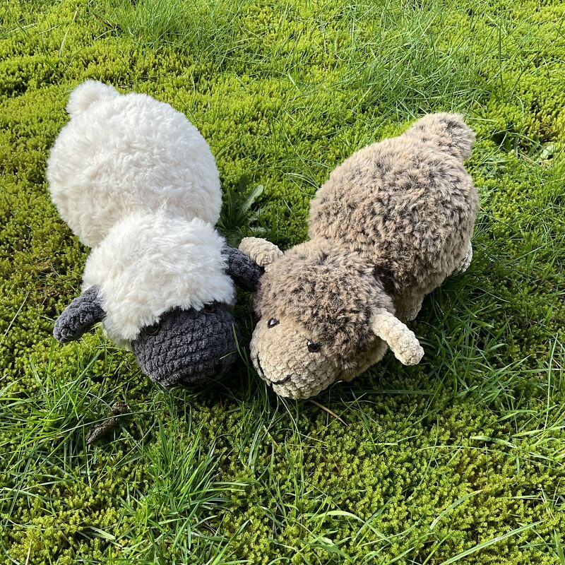 Kuschelige Amigurumi-Schafe in Naturtönen nebeneinander auf grünem Gras