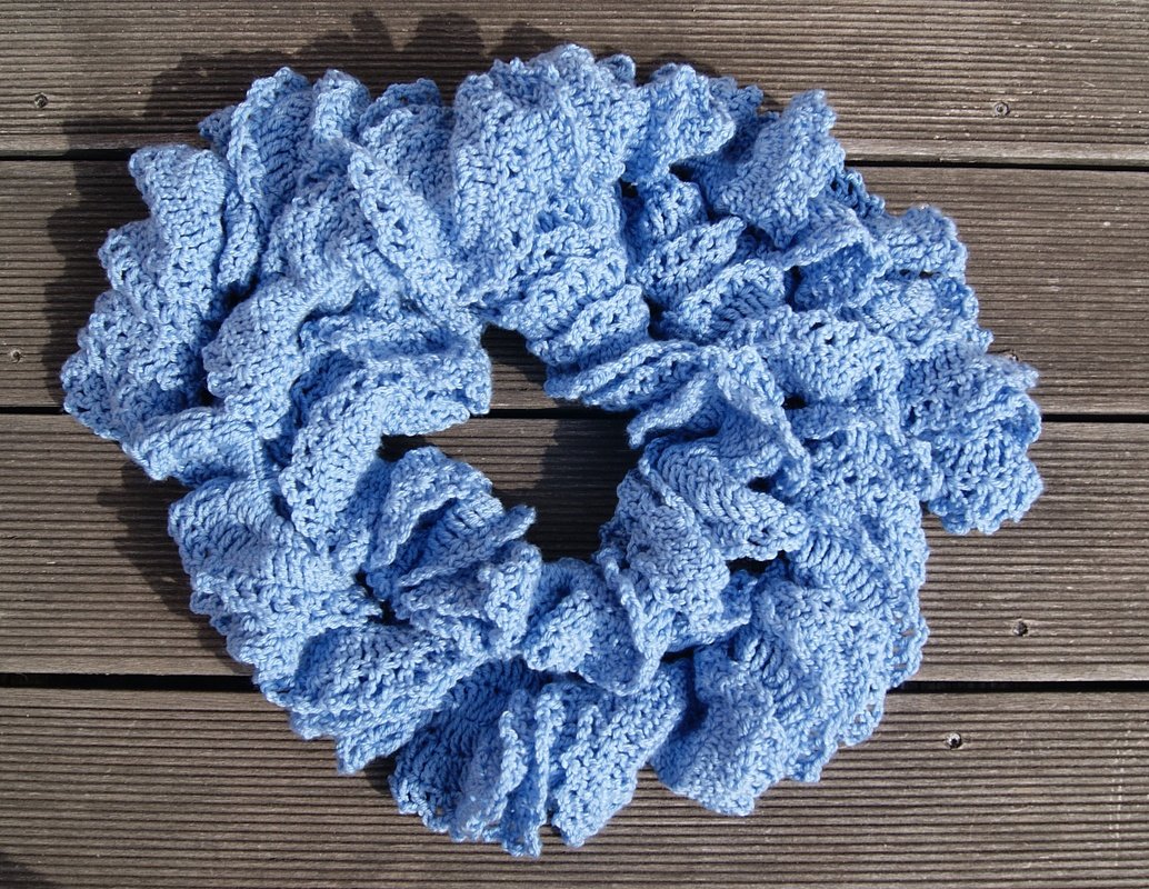 Hellblauer gehäkelter Schal mit Rüschen, liegend auf Holzdielen