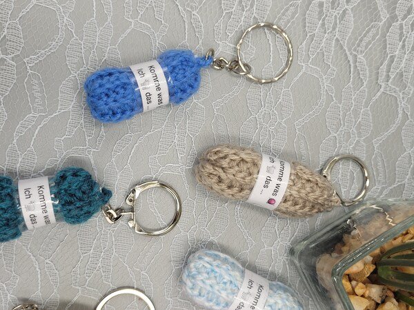 Mehrere gehäkelte Mini-Hausschuhe-Schlüsselanhänger in Blau, Türkis und Beige auf weißer Spitze