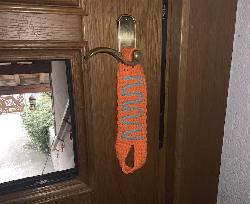 Orange gehäkelter Türstopper mit blauer Zickzack-Bordüre hängt an Türgriff