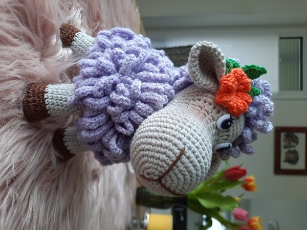 Amigurumi‑Schaf gehäkelt, lila gelockter Körper, grauer Kopf, orangefarbene Blüte
