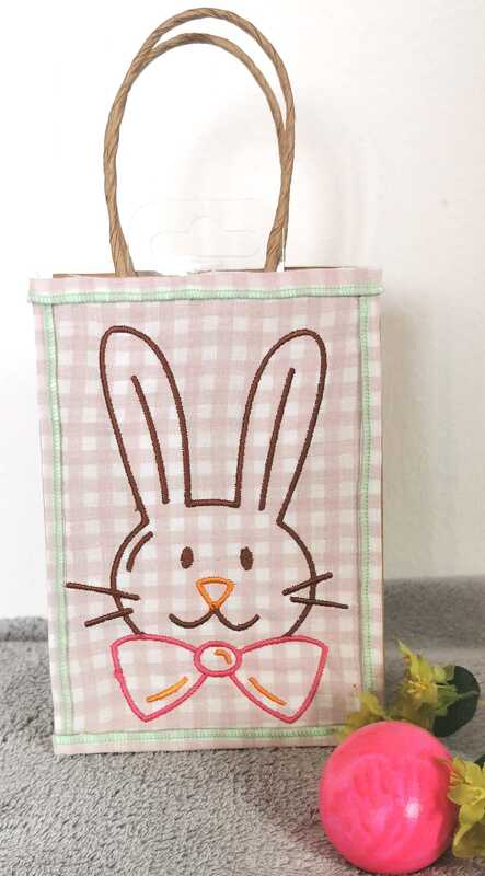 Rosa-weiß kariertes Täschchen mit gesticktem Hasenkopf und rosa Schleife, daneben ein rosa Osterei