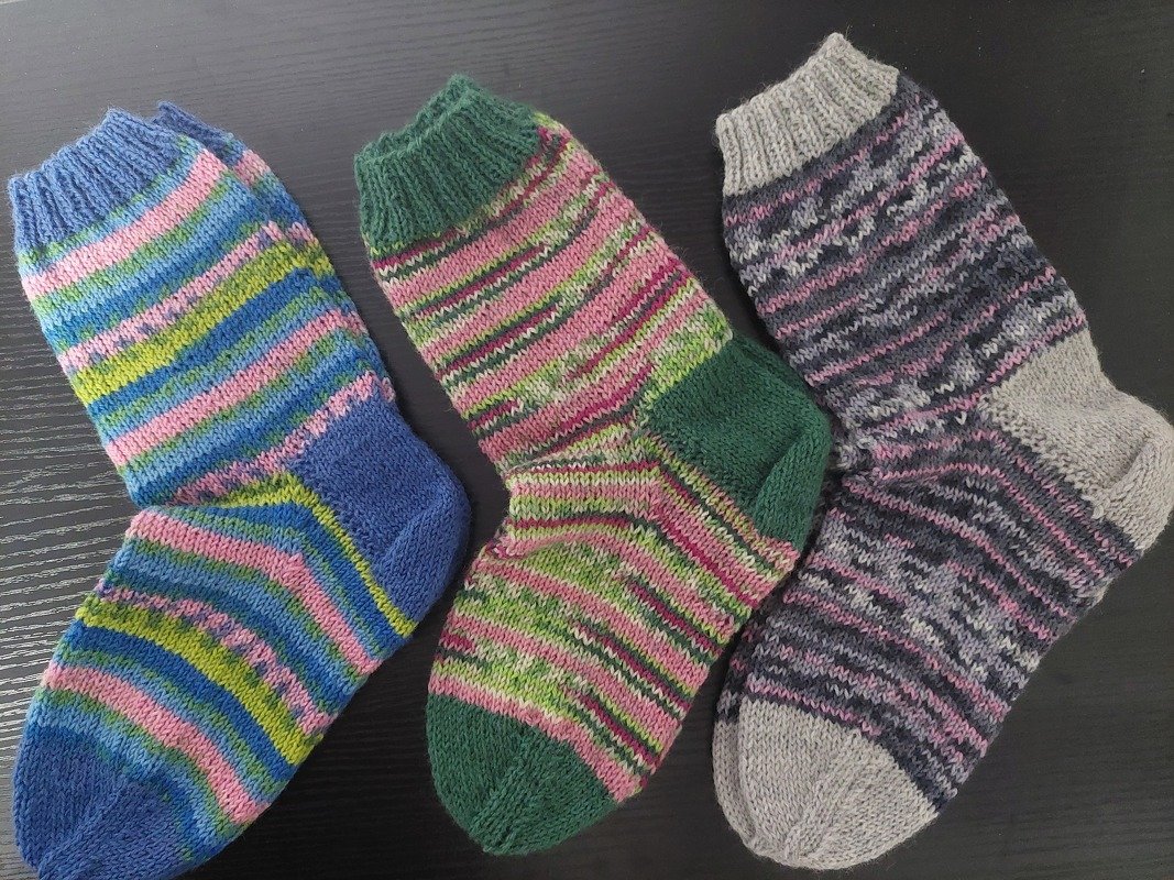 Drei Paare gestrickter Socken mit bunten Streifenmustern: blau, grün und grau.