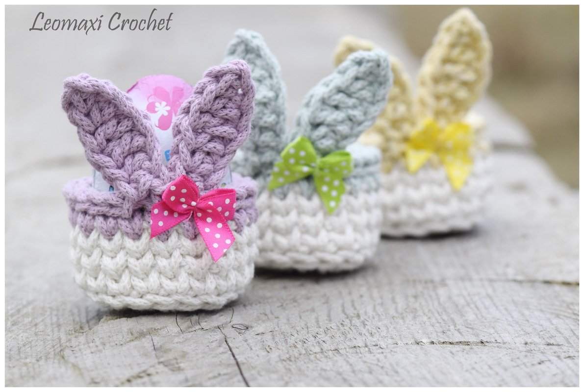 Drei gehäkelte Osterkörbchen mit Hasenohren und gepunkteten Schleifen auf Holz