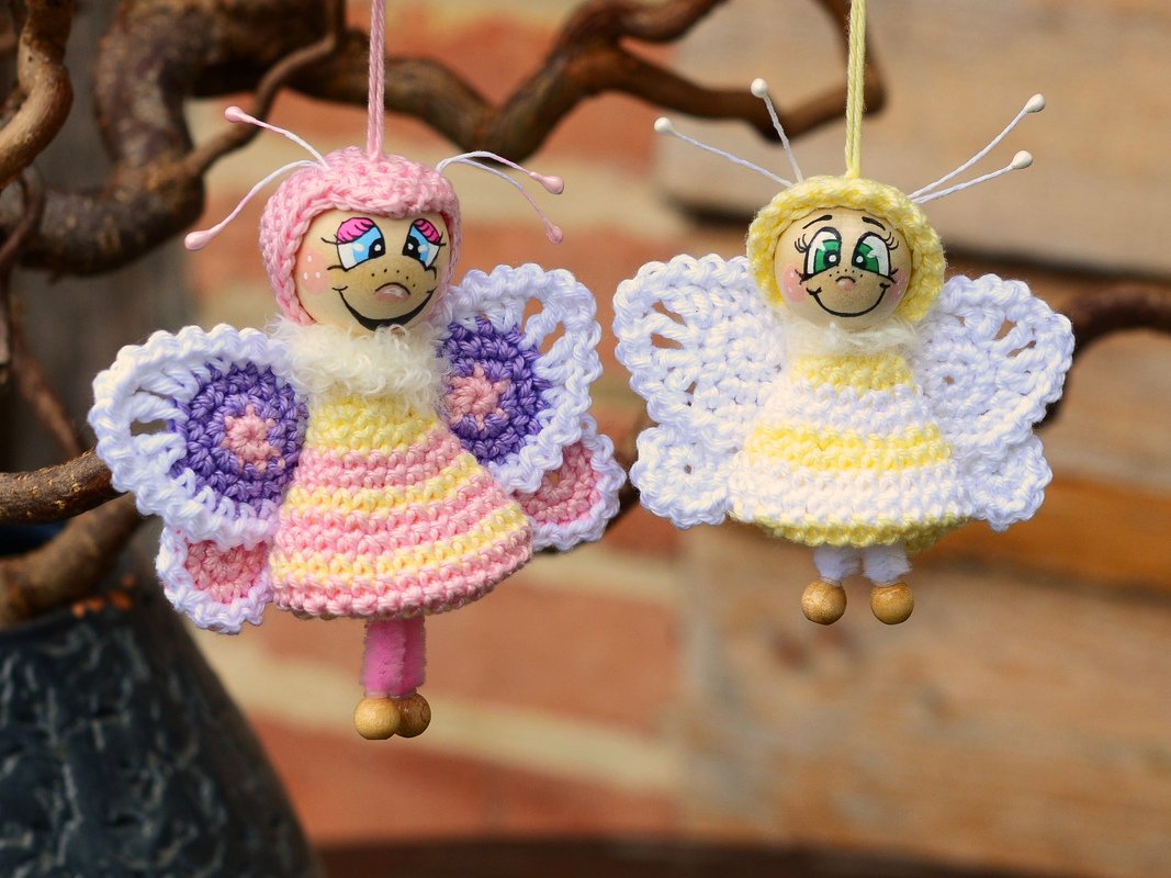 Zwei pastellfarbene Amigurumi-Schmetterlinge mit bemalten Holzköpfen und gehäkelten Flügeln