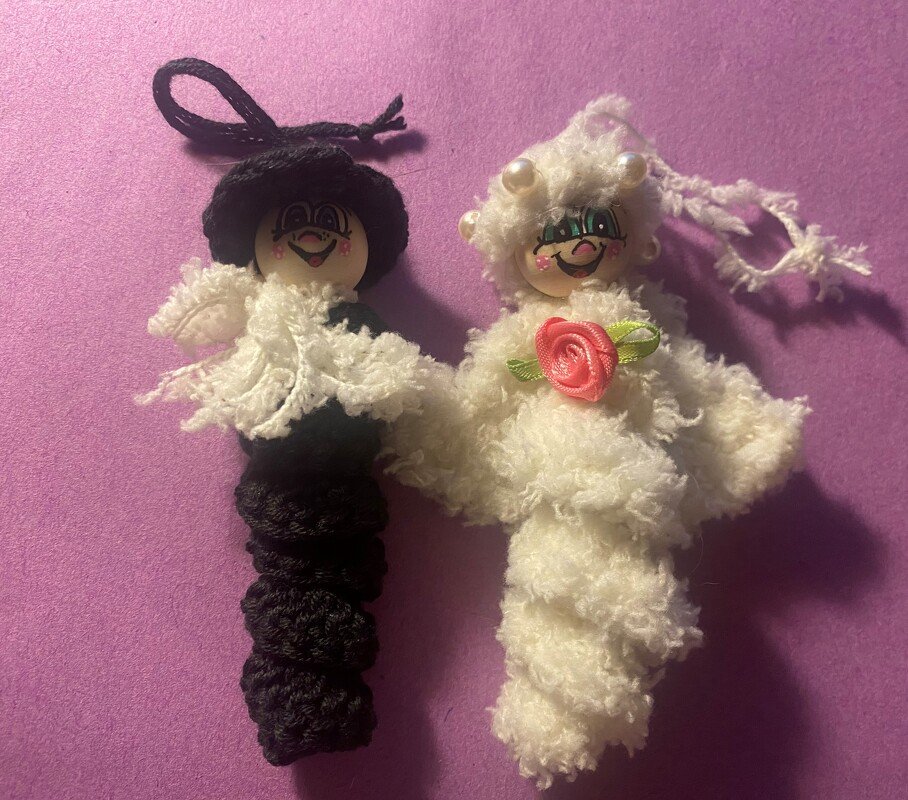 Zwei gehäkelte Anhänger in Schwarz und Weiß mit bemalten Holzperlenköpfen, Perlen und Rosen-Applikation auf violettem Hintergrund