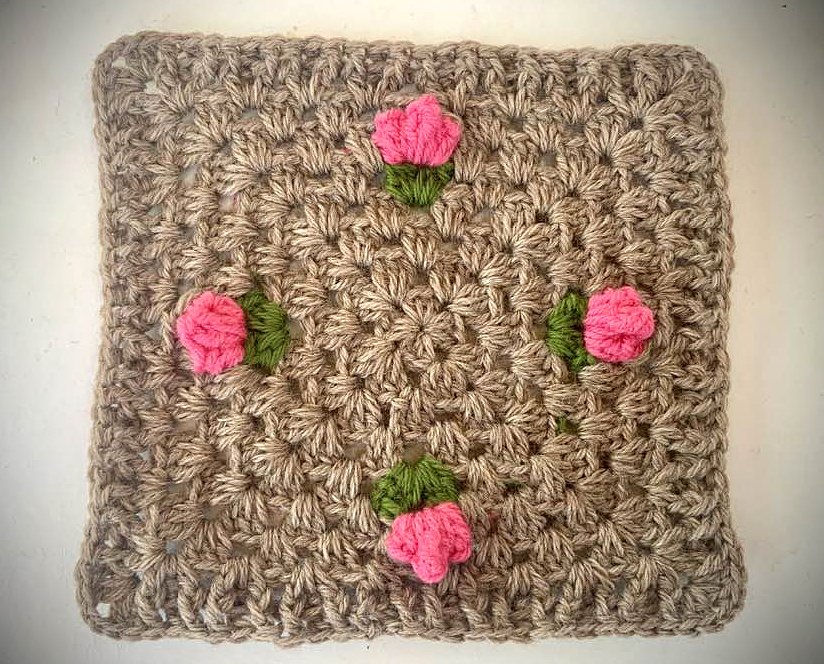 Beiges Granny Square mit vier applizierten rosa Rosen und grünen Blättern