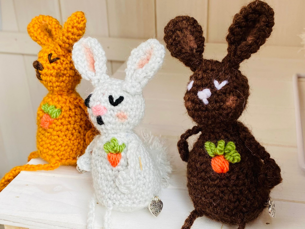 Handgehäkelte Osterhasen aus Garn in Gelb, Weiß und Braun mit gestickten Karottenmotiven