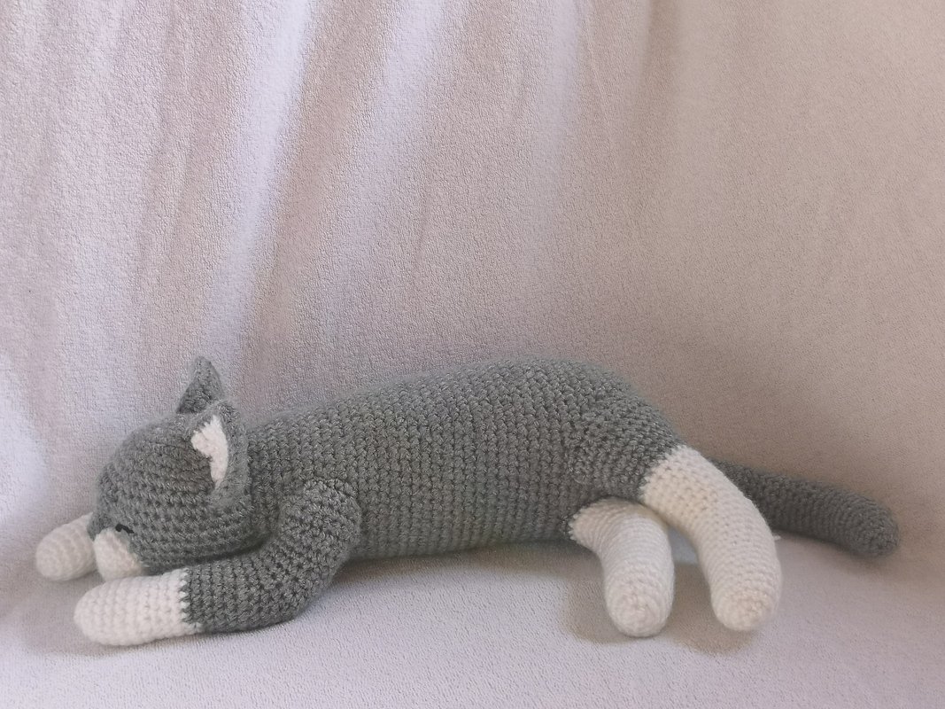 Grey and white crocheted amigurumi cat lying on its side, sleeping