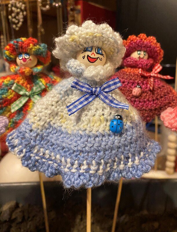 Drei gehäkelte Deko-Figuren auf Holzstäben, mittlere mit blau-weißem Kleid und Marienkäfer