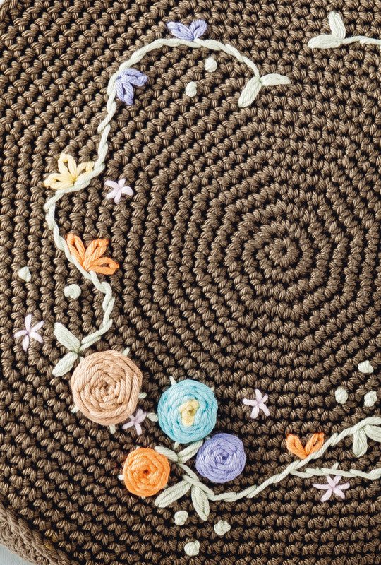 Runde braune Häkelstruktur mit pastellfarbenen gestickten Blumen und Blättern