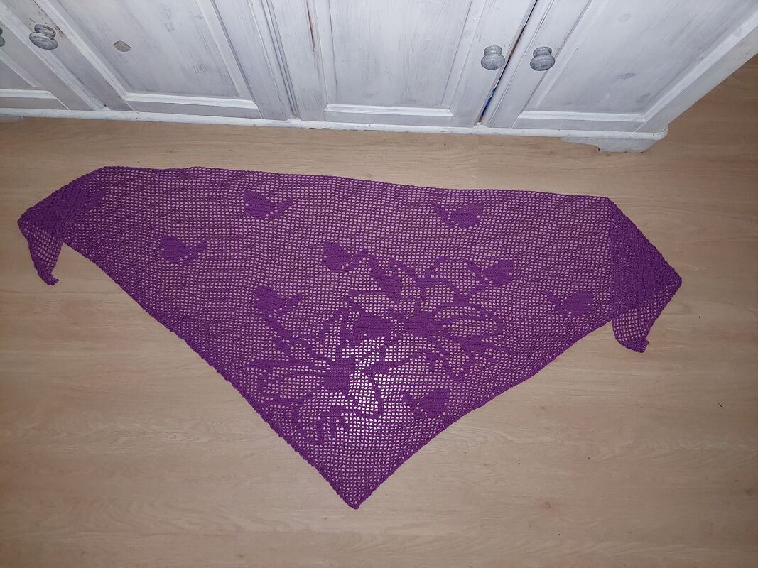 Lila gehäkeltes Dreieckstuch mit Herz- und Blumenmotiv, flach auf dem Boden ausgelegt