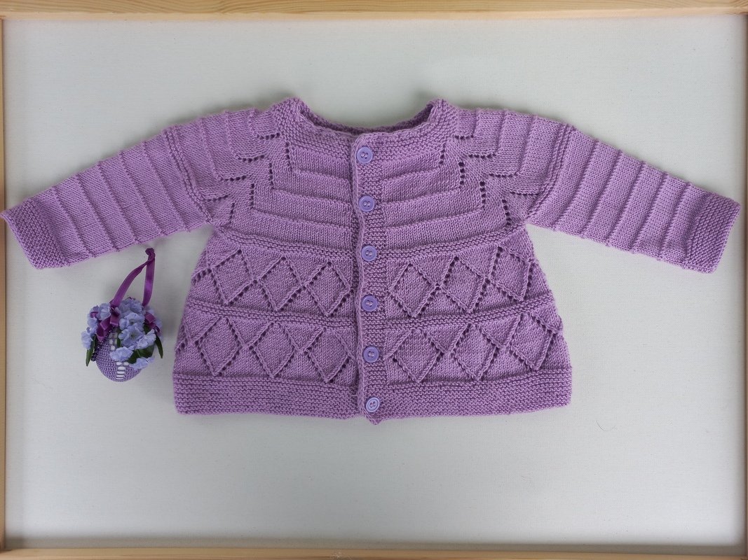 Fliederfarbene, gestrickte Babyjacke mit Knopfleiste und Rautenmuster, flach liegend fotografiert