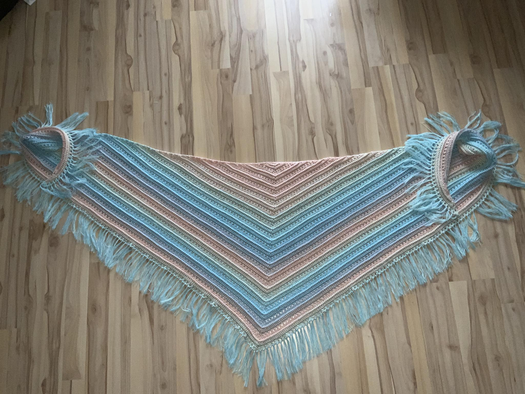 Gehäkeltes Dreieckstuch mit pastellfarbenen Streifen, Fransen und sichtbaren Schlaufen, flach auf Holzboden ausgelegt