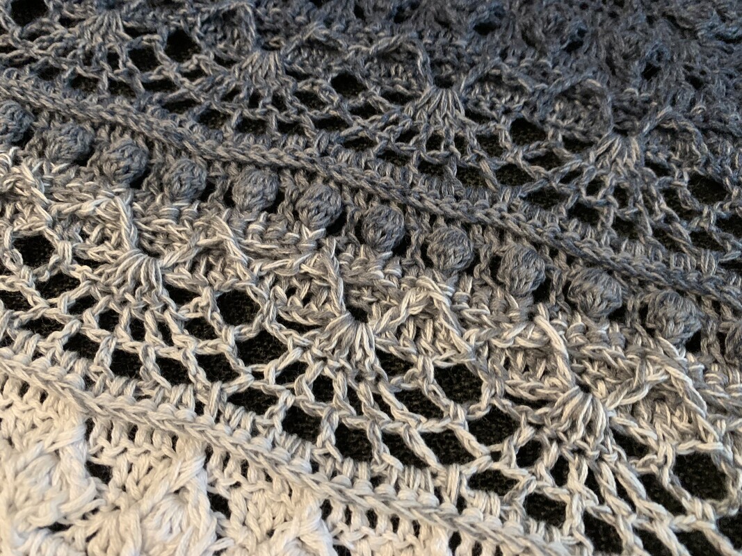 Close-up of a grey ombré crochet triangle shawl with lace mesh, shell motifs and bobble stitch row