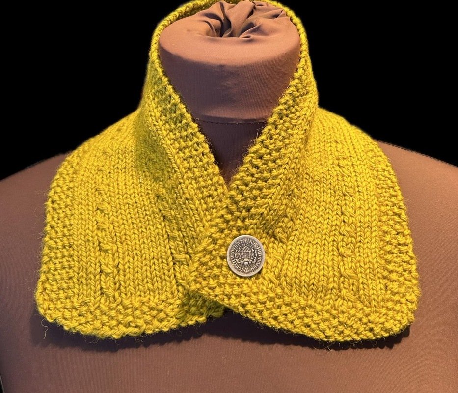 Senfgelber gestrickter Kragen mit dekorativem Knopf auf einer braunen Büste.