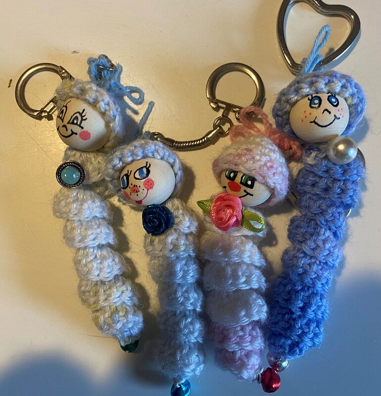 Vier handgehäkelte Schlüsselanhänger in Weiß, Blau und Rosa mit Holzperlenköpfen und aufgemalten Gesichtern