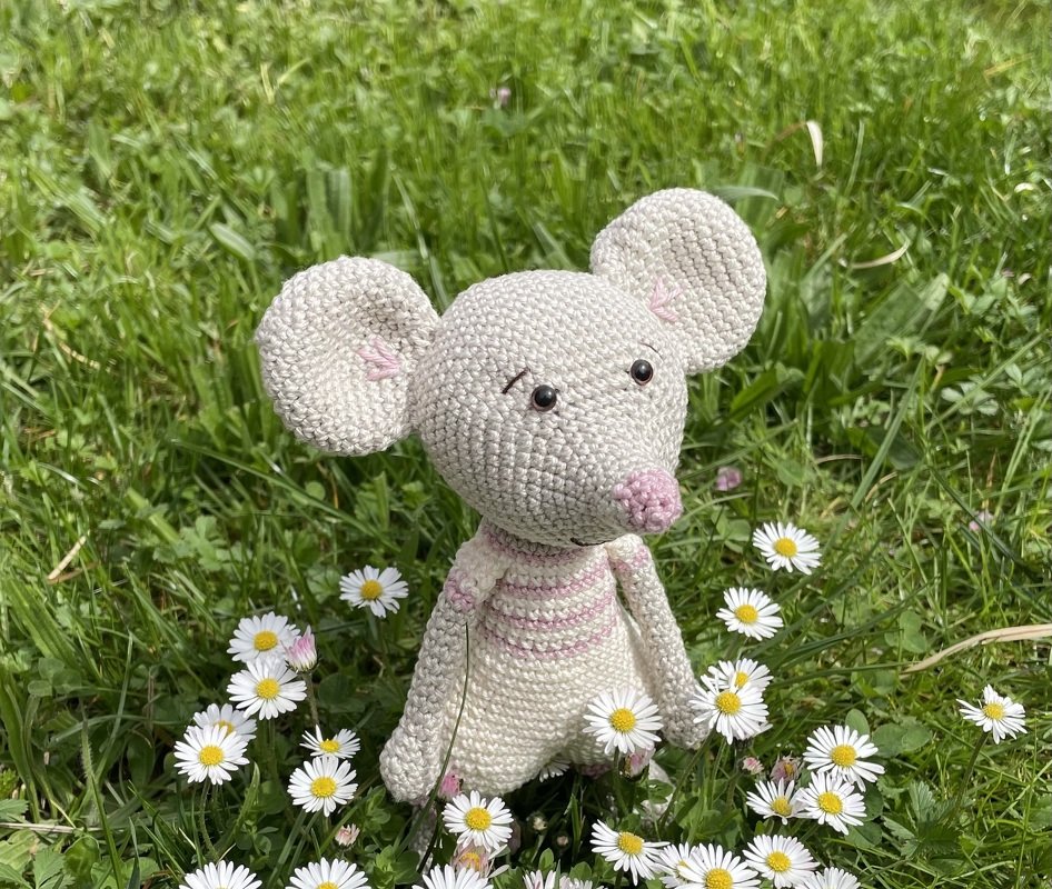 Nahaufnahme einer gehäkelten Amigurumi‑Maus mit großen Ohren und gestickter Nase im Gras