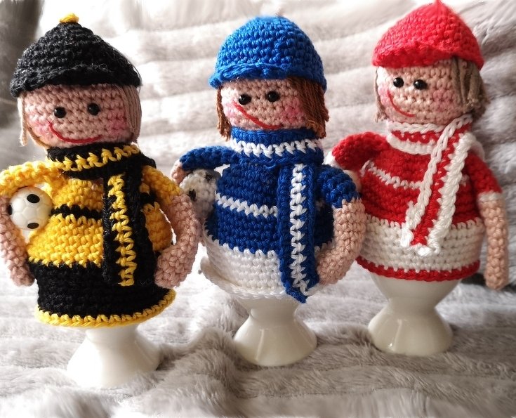 Bunte gehäkelte Eierwärmer-Figuren mit Mützen und Schals auf Eierbechern