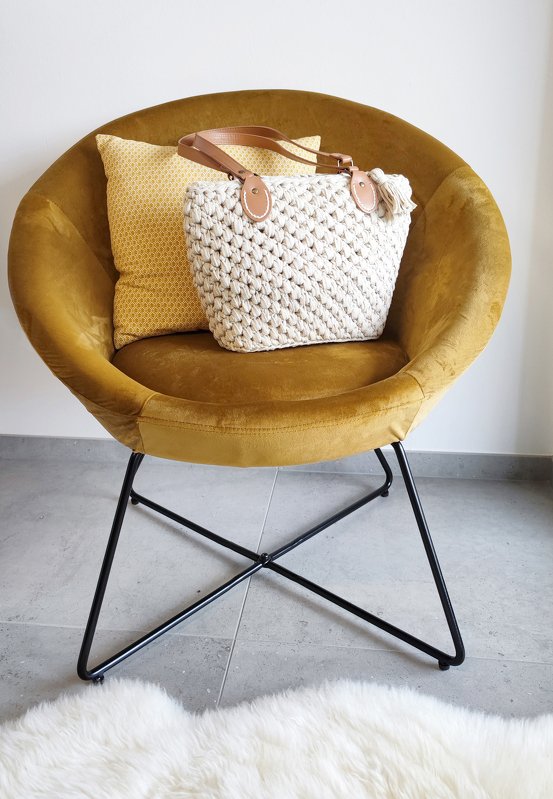 Boho-inspirierte gehäkelte Henkeltasche in Creme mit Quaste auf senffarbenem Stuhl