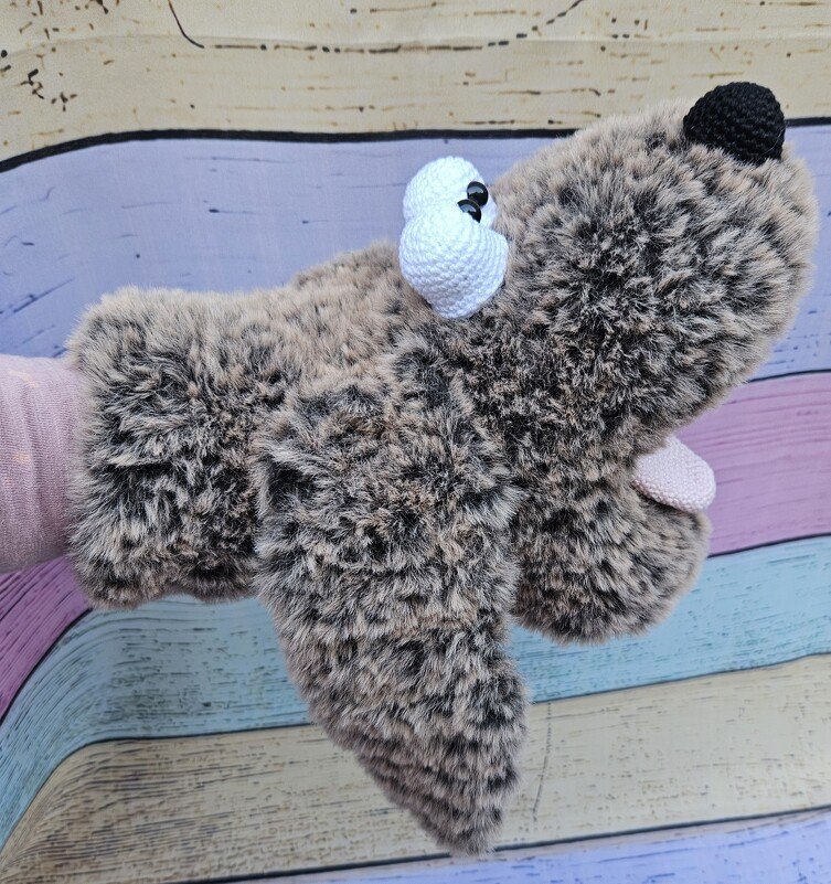 Nahaufnahme brauner flauschiger Amigurumi-Handpuppe mit weißen gehäkelten Augen, schwarzer Nase und rosa Zunge