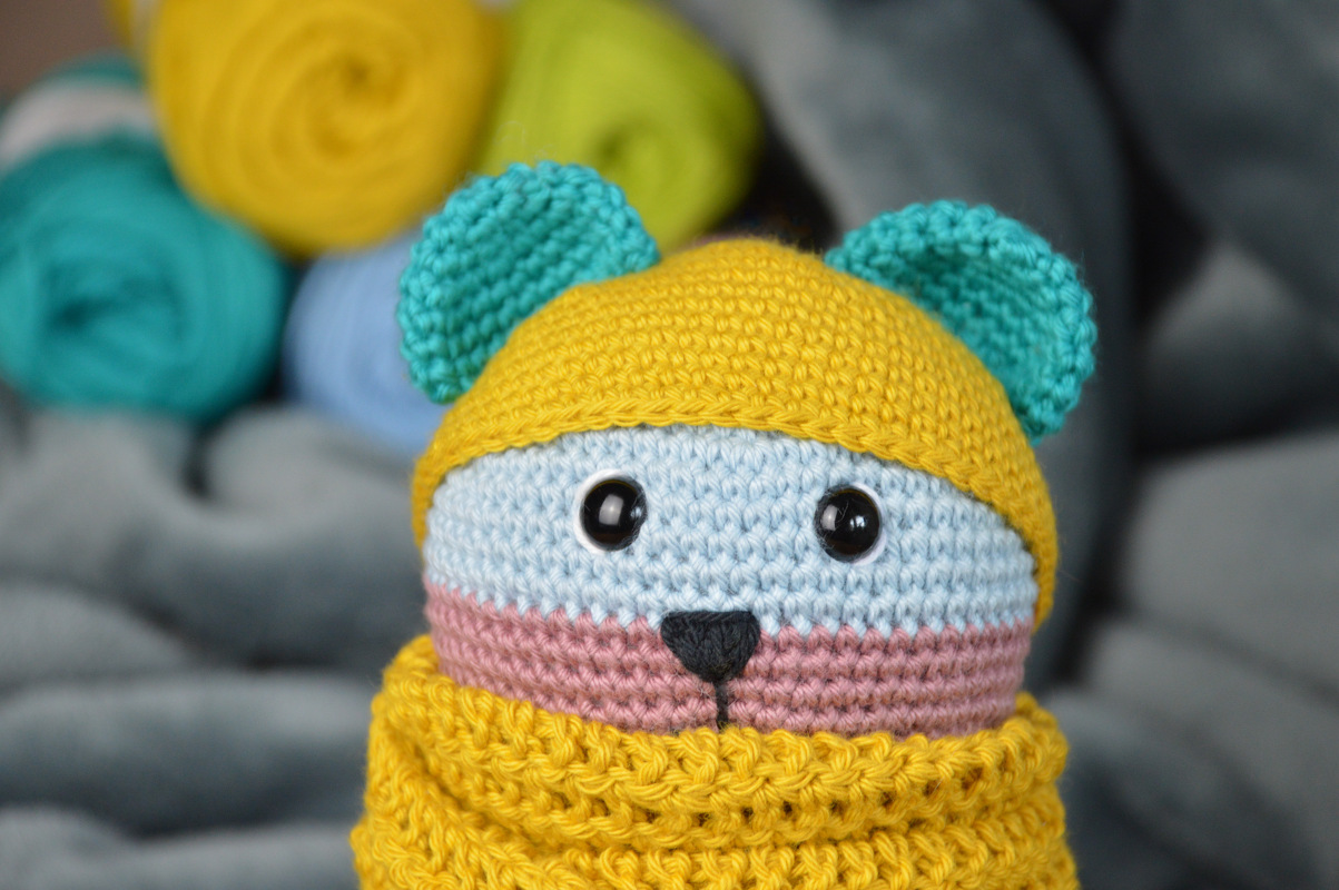 Gehäkelte Amigurumi-Figur mit gelber Mütze, türkisfarbenen Ohren und gelbem Schal