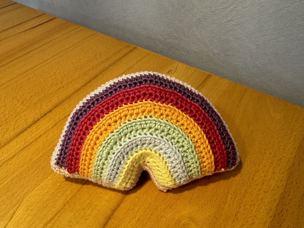 Gehäkelter Regenbogen mit bunten Streifen auf Holztisch