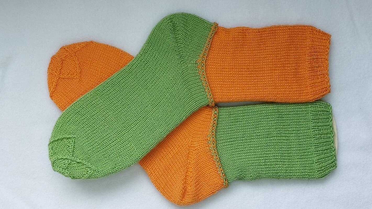 Zwei zweifarbige gestrickte Socken in Grün und Orange, übereinander liegend auf weißem Hintergrund