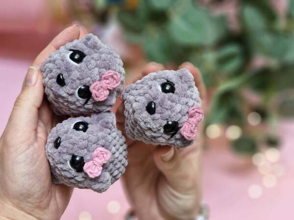 Hand holding three pocket-sized grey amigurumi mice with pink bows