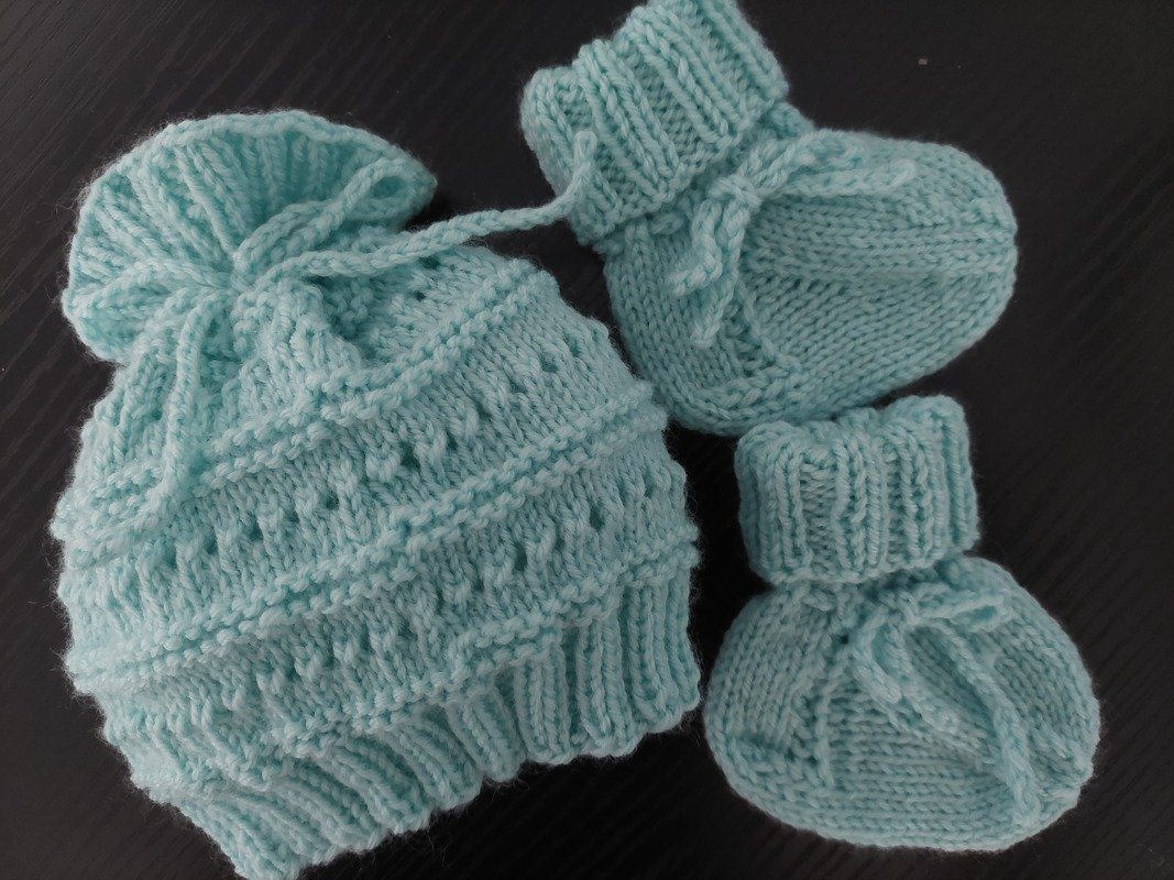 Gestrickte Baby-Mütze mit Kordel und zwei Schühchen in Mint auf dunklem Untergrund