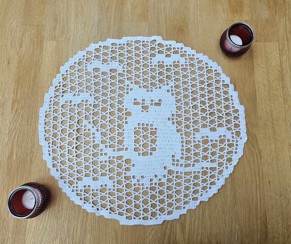 Rundes Filet-Häkeldeckchen mit Katzenmotiv auf hellem Holztisch, zwei Teelichthalter am Rand