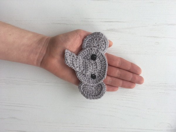 Small grey crocheted elephant head applique with black button eyes held in a hand