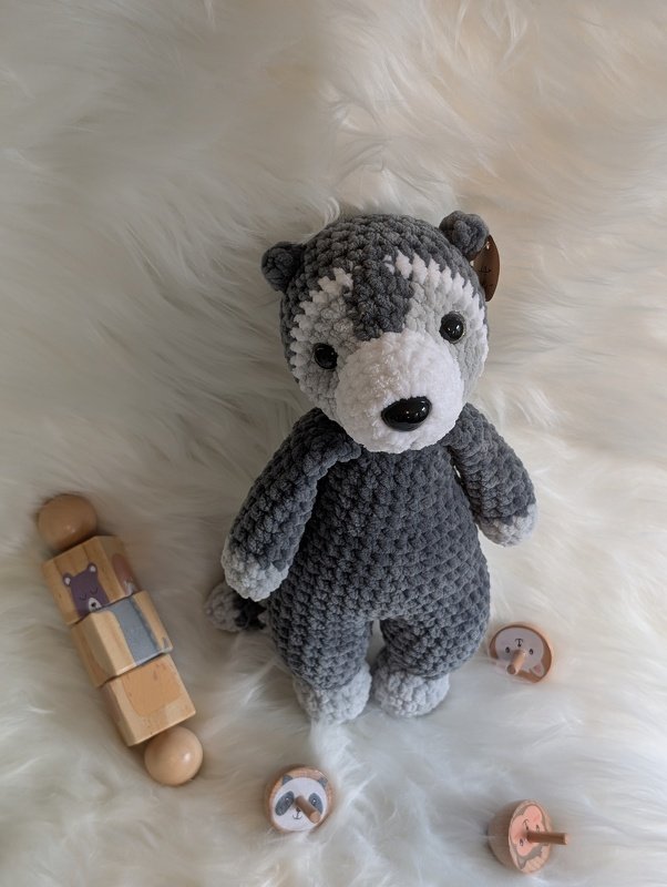 Gehäkeltes graues Amigurumi-Husky mit weißen Details auf hellem Fell, umgeben von Holzspielzeug