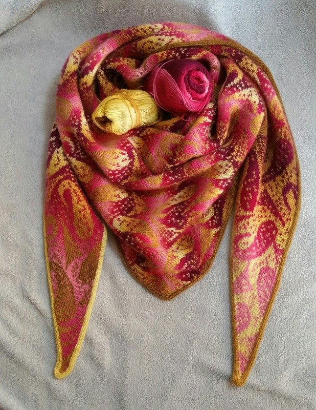 Gestricktes dreieckiges Tuch in Pink-, Magenta- und Gelbtönen mit gemustertem Farbverlauf und zwei Garnknäueln.