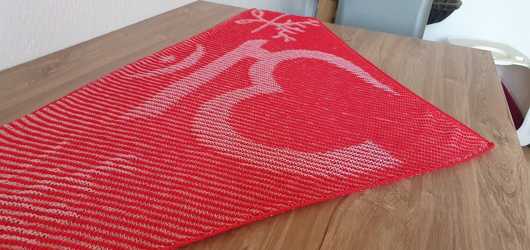 Red triangular knitted shawl with a white deer motif, laid flat on a wooden table.