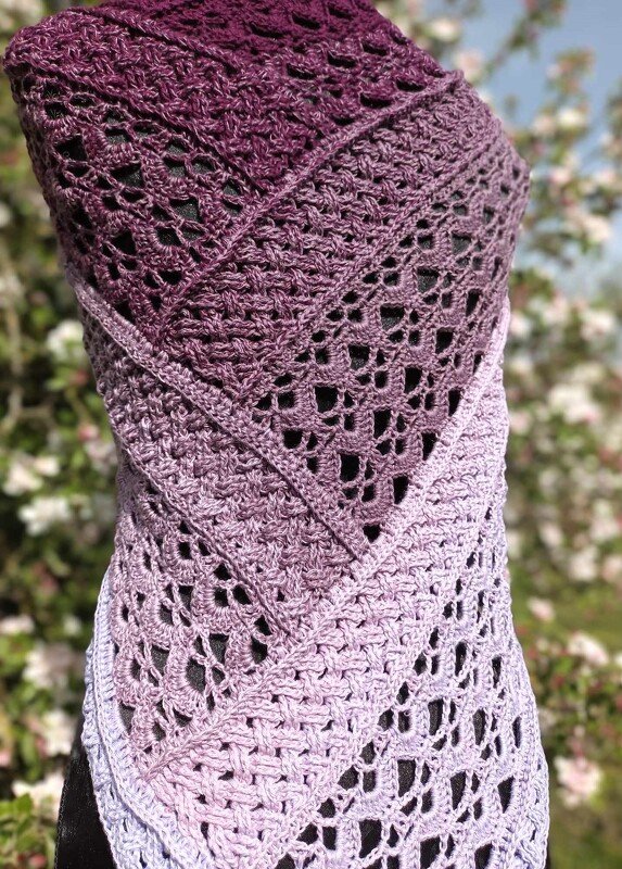 Close-up of triangle shawl showing lace motifs and textured stitch bands in a purple gradient